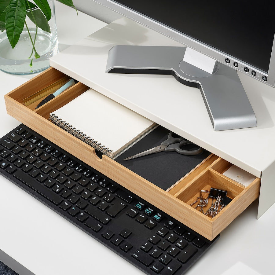 A white monitor stand with a drawer, measuring 10x47x26 cm. Made of durable bamboo with a white aluminum frame, it features compartments for organizing office supplies and a space to store a keyboard. The ergonomic design helps reduce neck and shoulder strain while providing cable management for a tidy workspace.